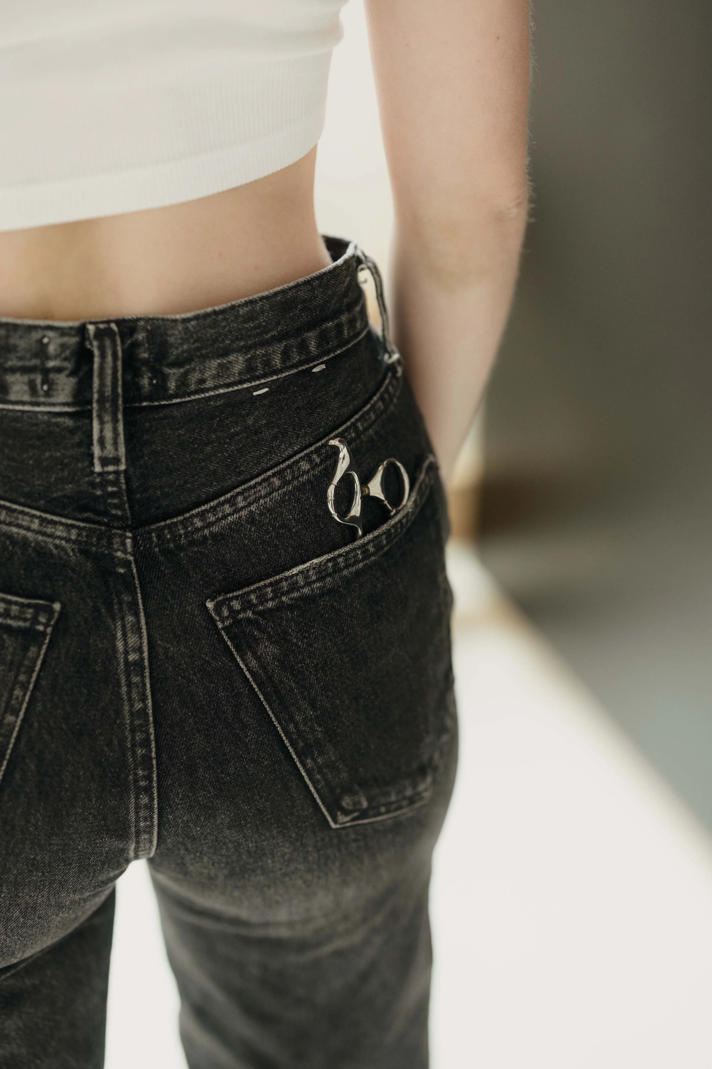 Close-up of a person wearing black high-waisted jeans and a white crop top, standing against a blurred background.