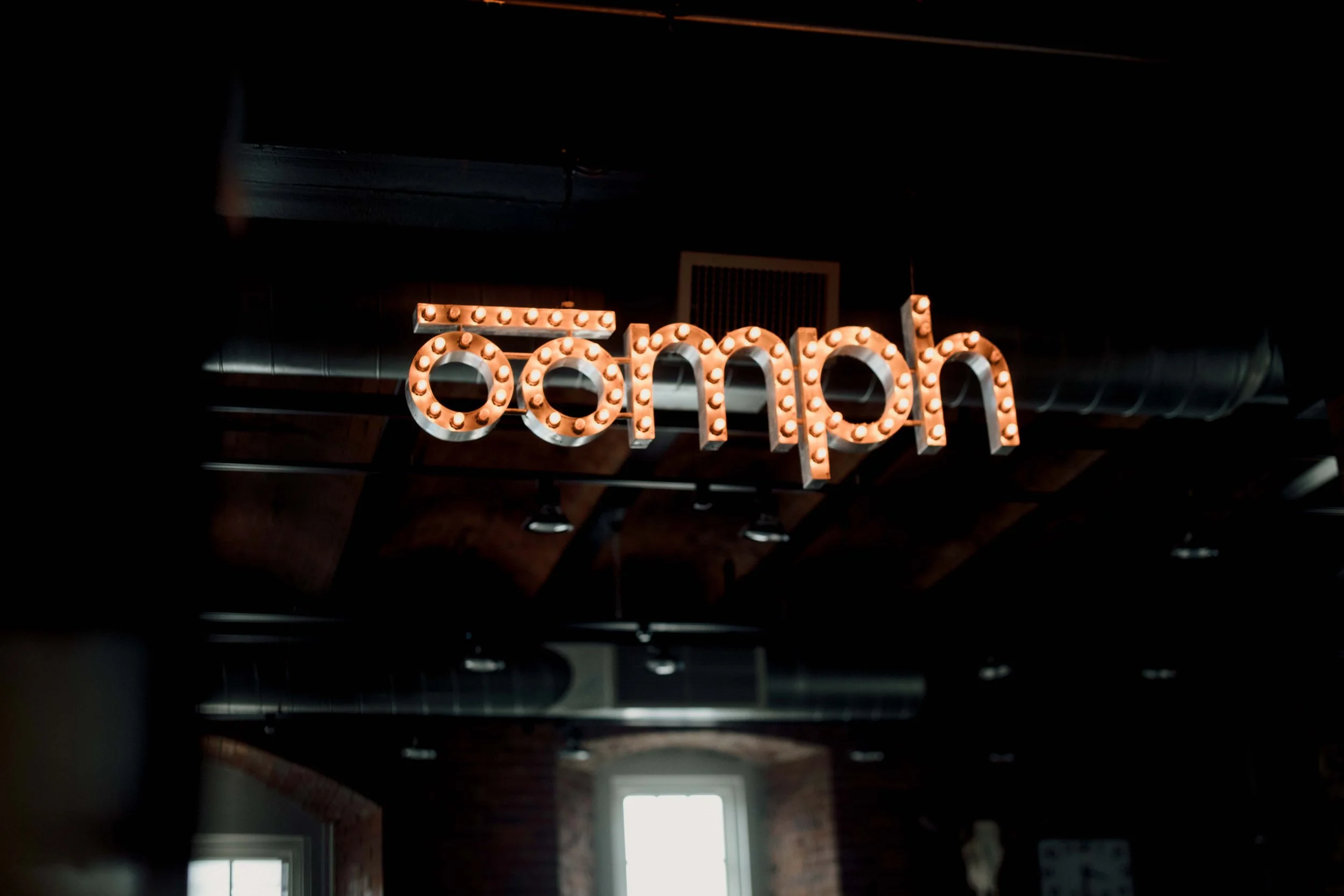 Illuminated sign spelling 'barrel' with individual light bulbs framing each letter, hanging from a ceiling in a dimly lit space.