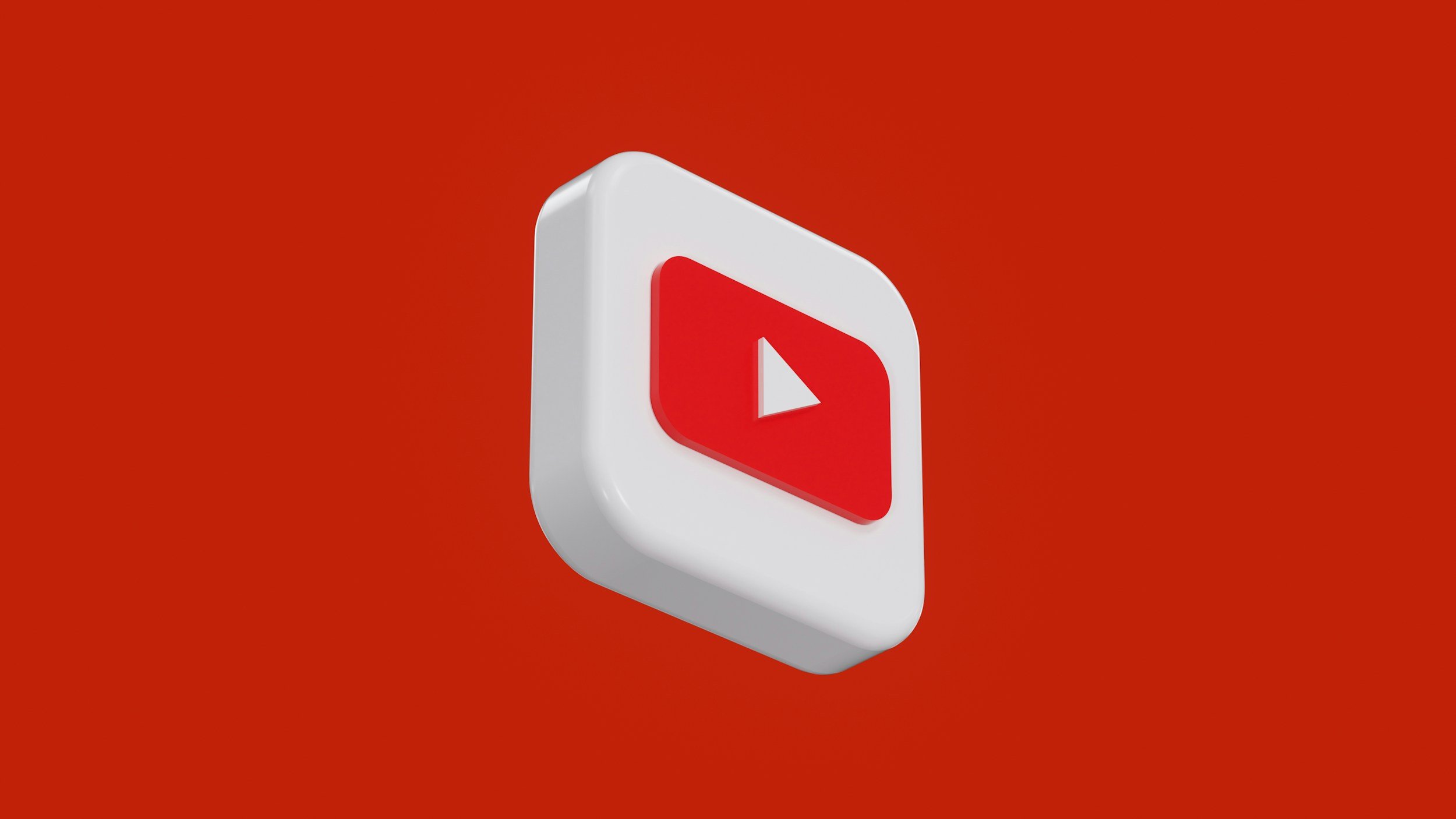 3D icon of a red YouTube play button on a white rectangular background with rounded edges, against a red background.