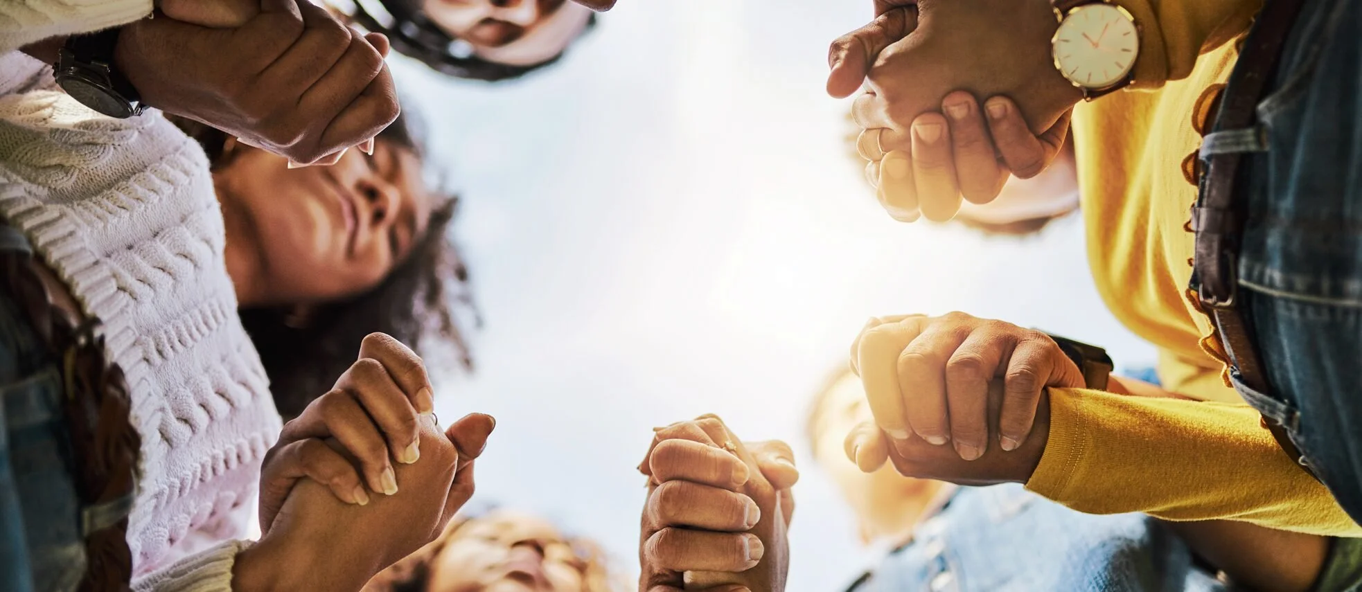 People in a close-up, low-angle view, engaged in a group activity, with their hands clasped and arms intertwined, symbolizing unity and teamwork.