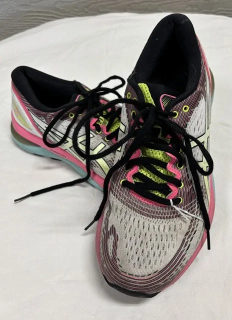 A pair of black Nike sneakers with yellow branding and accents, resting on a pink spiked roller skate blade with metal spikes, on a white wire shelf.
