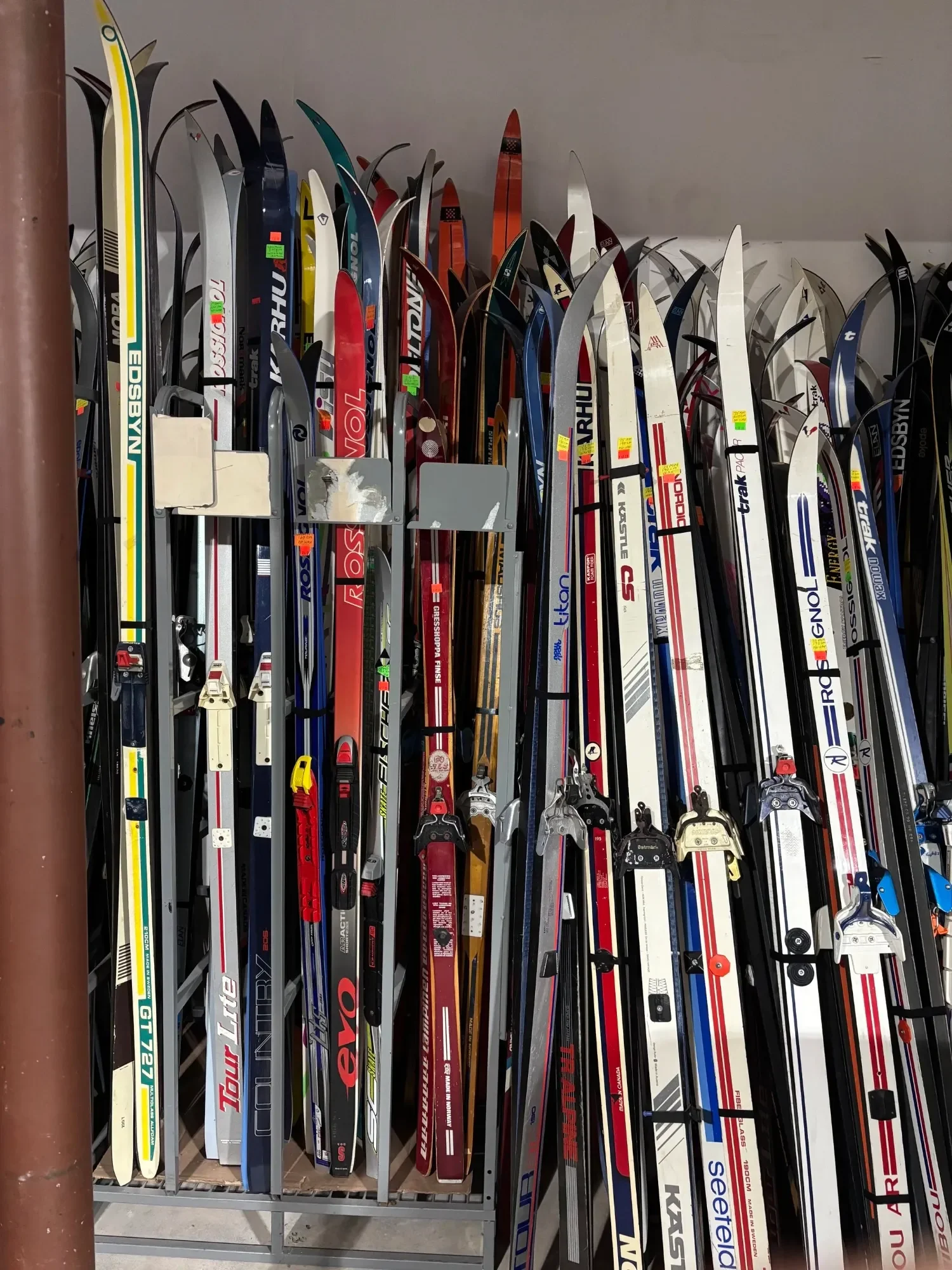 A collection of numerous cross-country skis stored upright on a metal rack, displaying various colors, brands, and designs.