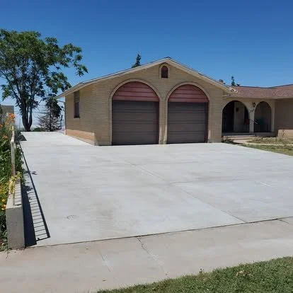 Residential driveway and garage with two closed garage doors, brick exterior, and a small porch area under a sunny blue sky.