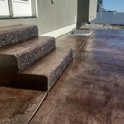 Stained concrete steps and concrete walkway next to a house with siding.