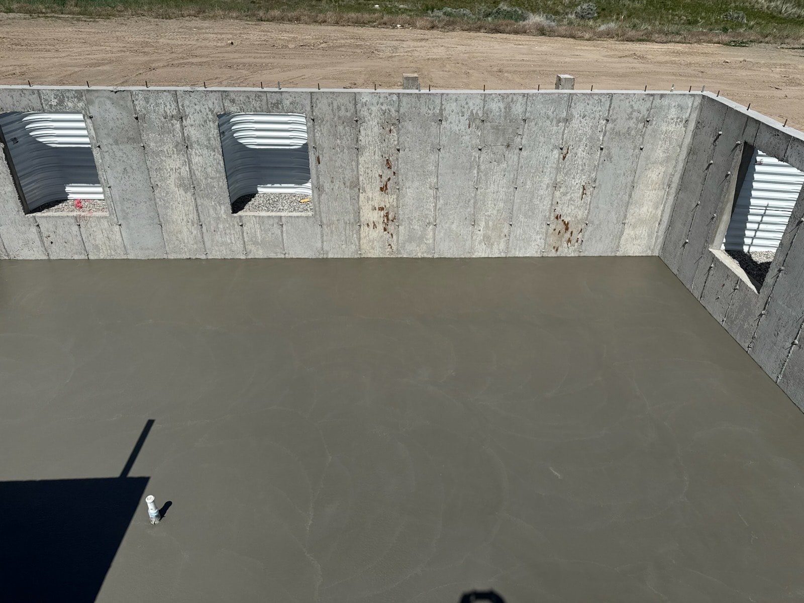 Fresh concrete floor inside a foundation wall area with a smooth finish and visible wall openings.