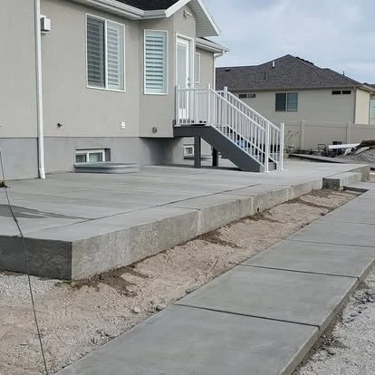 Finished concrete patio and walkway with clean control joints, a smooth surface, and a raised patio area beside the home.