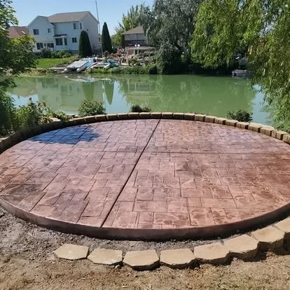 Decorative stamped concrete patio with a rounded design, rich color, and a finished border overlooking the water.