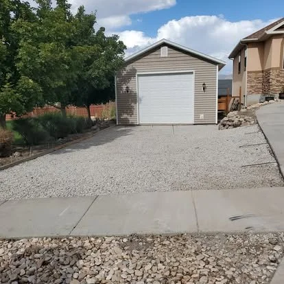 Driveway area before concrete installation, showing the gravel base and layout leading to a detached garage.