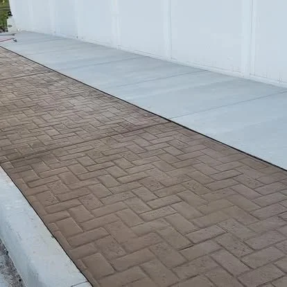 Finished stamped concrete walkway with a brick pattern, clean borders, and a smooth transition beside the driveway.