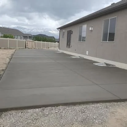 Finished backyard concrete patio with clean control joints, smooth edges, and a large usable surface beside the home.