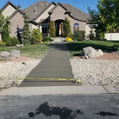Finished front concrete walkway leading to the home, with clean edges, control joints, and landscape rock on both sides.