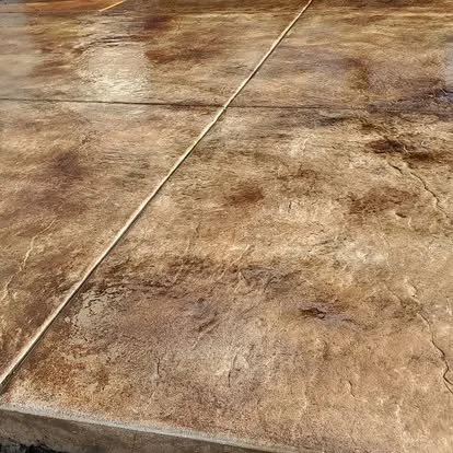 Close-up of stained decorative concrete showing warm color variation, control joints, and a textured sealed finish.