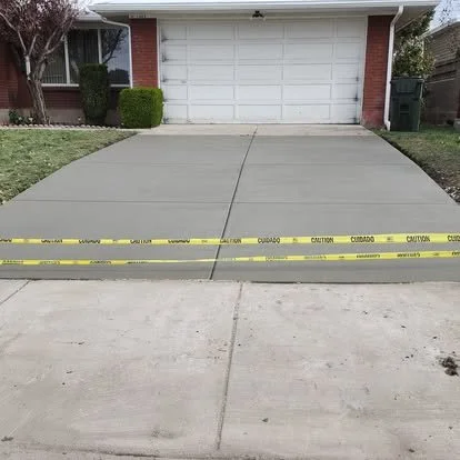 Completed residential concrete driveway with clean control joints and caution tape protecting the surface while it cures.