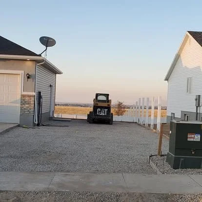 RV pad or side-yard parking preparation with compacted gravel base and equipment on-site before concrete installation.