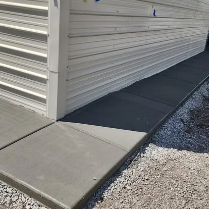 Concrete sidewalk leading to a metal-sided building with a small ramp for access.