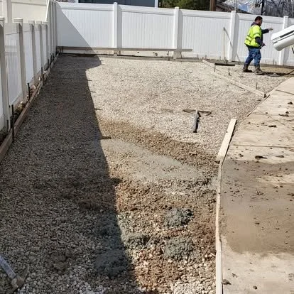 Side-yard concrete preparation with gravel base, forms, and grading work underway before the pour.