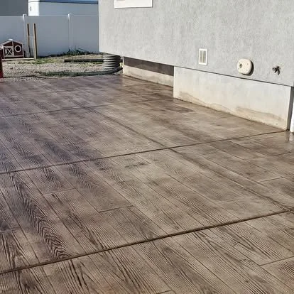 Wood plank stamped concrete patio with rich coloring, clean control joints, and a finished outdoor surface beside the home.