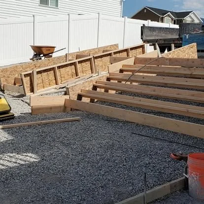 Concrete patio and stair project in progress with wood forms, gravel base, and step framing prepared for installation.