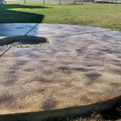 Rounded decorative concrete patio and fire pit with warm color variation, stamped texture, and a clean finished edge.
