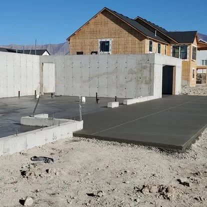 Construction site with fresh concrete foundation and a partially built house in the background.
