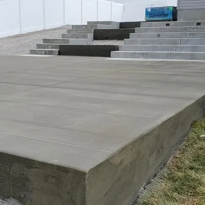 Concrete outdoor stairs with multiple steps leading up to a structure, with part of a grassy area visible.