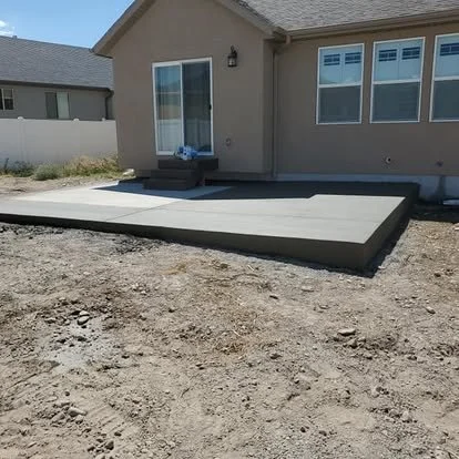Finished backyard concrete patio extension with clean edges, smooth finish, and a raised step area near the home.