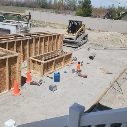 Concrete patio and stair project in progress with wood forms, equipment, and site preparation for a custom outdoor space.