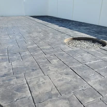 Finished gray stamped concrete patio with a fire pit, stone-style pattern, clean layout, and decorative gravel accents.