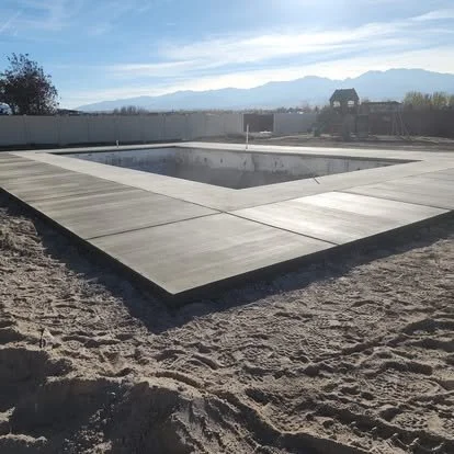 Large newly finished concrete pad pool surround with clean edges and control joints, creating a defined outdoor space.