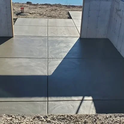 Concrete pathway leading to a construction site with dirt and gravel, partially shaded.