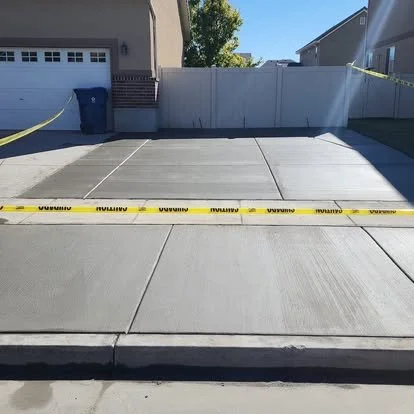 Newly poured concrete driveway with clean edges, control joints, and caution tape protecting the finished surface.