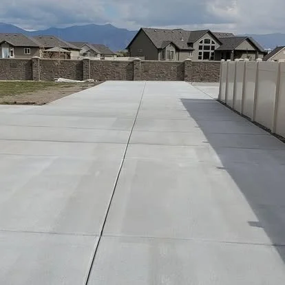 Concrete driveway leading to a residential backyard with houses and mountains in the background.