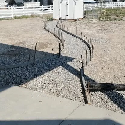 A curved wooden frame on a construction site, with gravel inside and metal stakes supporting the shape.