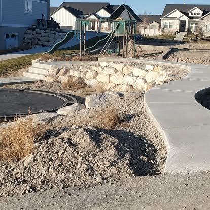 Curved concrete walkway and patio area in progress with landscape rock, gravel base, and custom outdoor layout work.