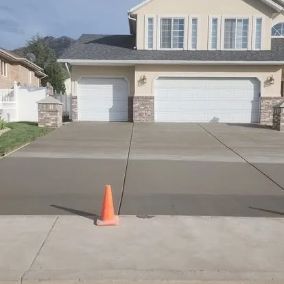 Empty concrete driveway with a traffic cone in the foreground and a residential house with two garages in the background.