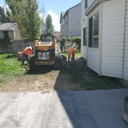 Concrete preparation work in progress between homes, with equipment used to clear and prep the area for installation.