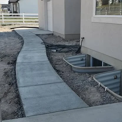Finished curved concrete walkway beside the home with clean edges and a smooth residential finish.