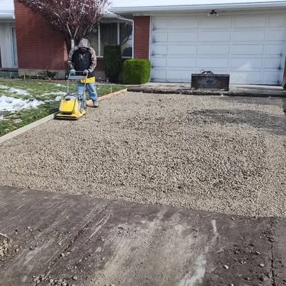 Driveway base preparation using compaction equipment to create a solid foundation before concrete is poured.