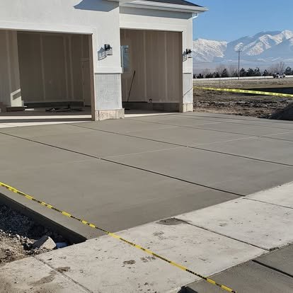 Newly poured concrete driveway in front of a garage with mountains in the background under a clear blue sky.