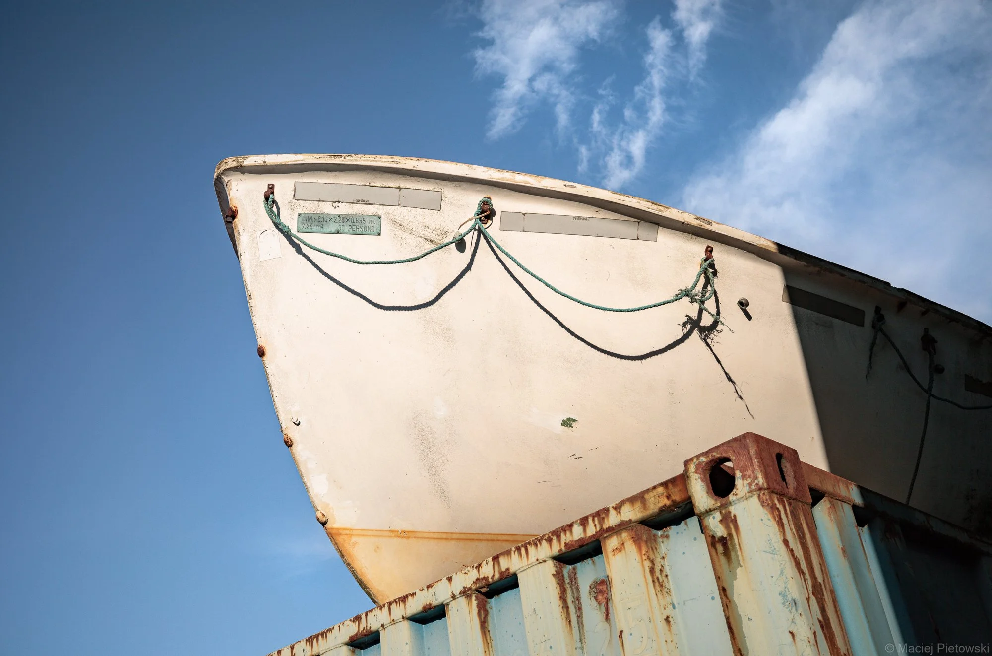 Close-up of a weathered, rusty boat or ship partially on a rusted metal surface under a partly cloudy blue sky.
