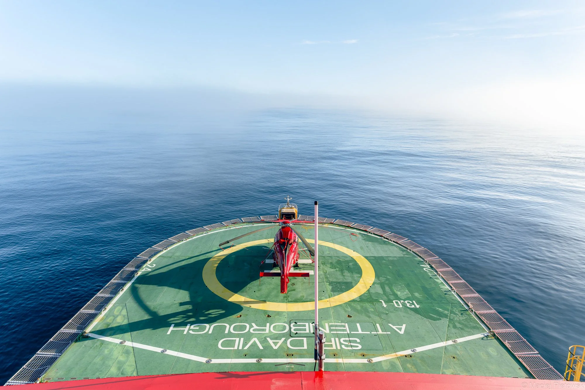 View from a helicopter deck over calm blue ocean with a clear sky.