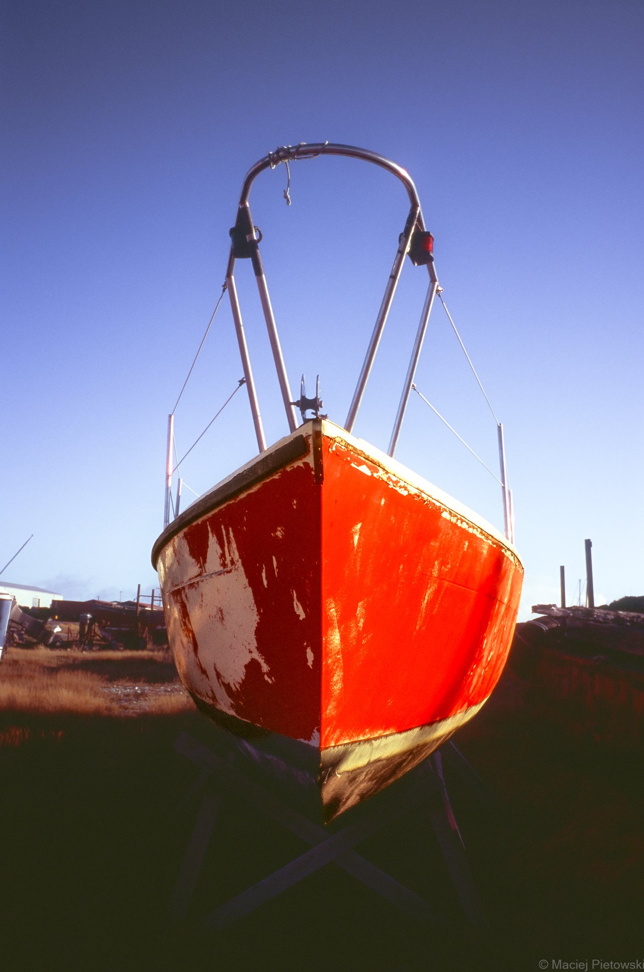 Front view of a red boat on land with a clear sky background.