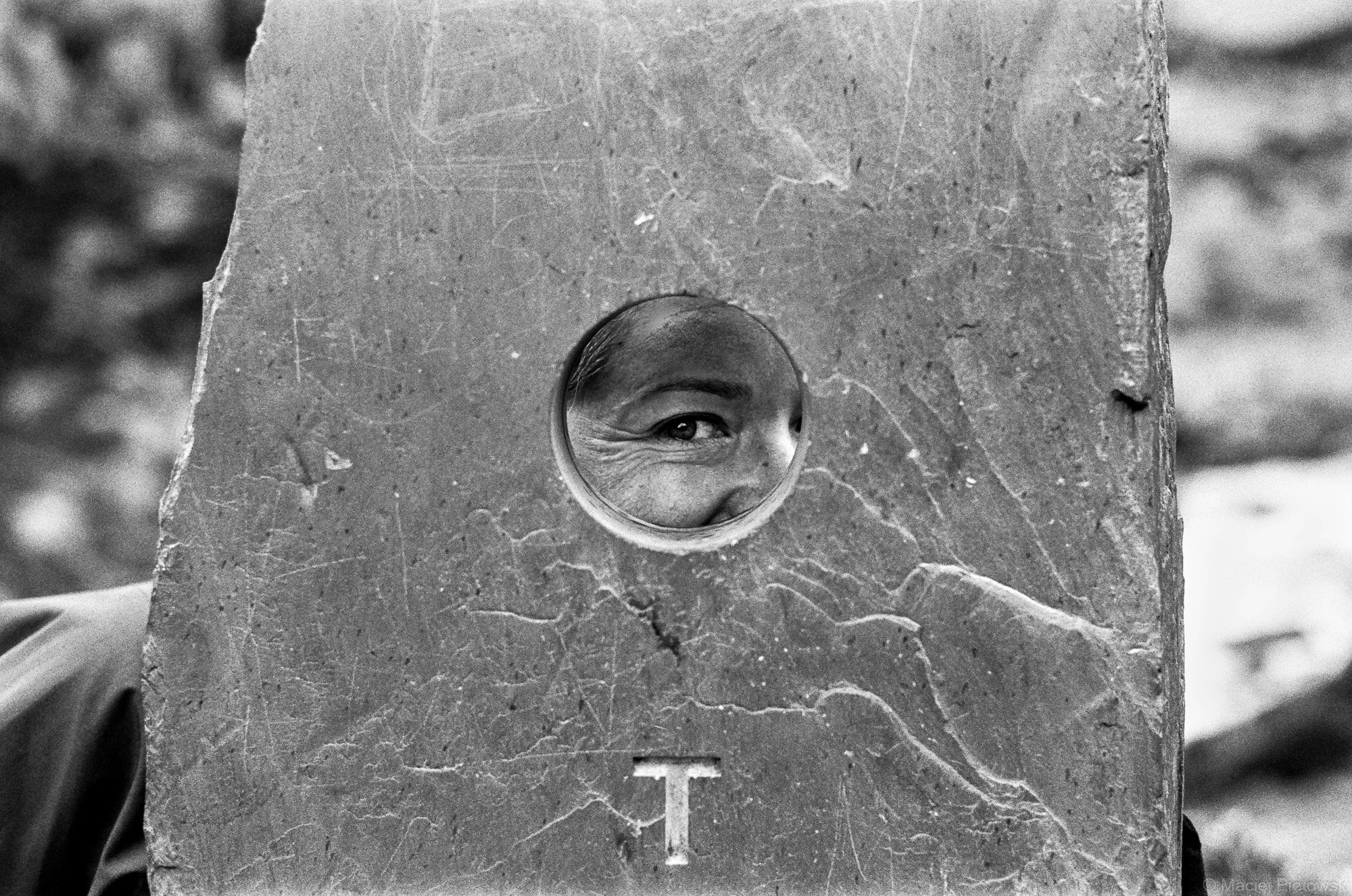 A person looking through a circular hole in a large stone slab, with a smile visible through the hole.
