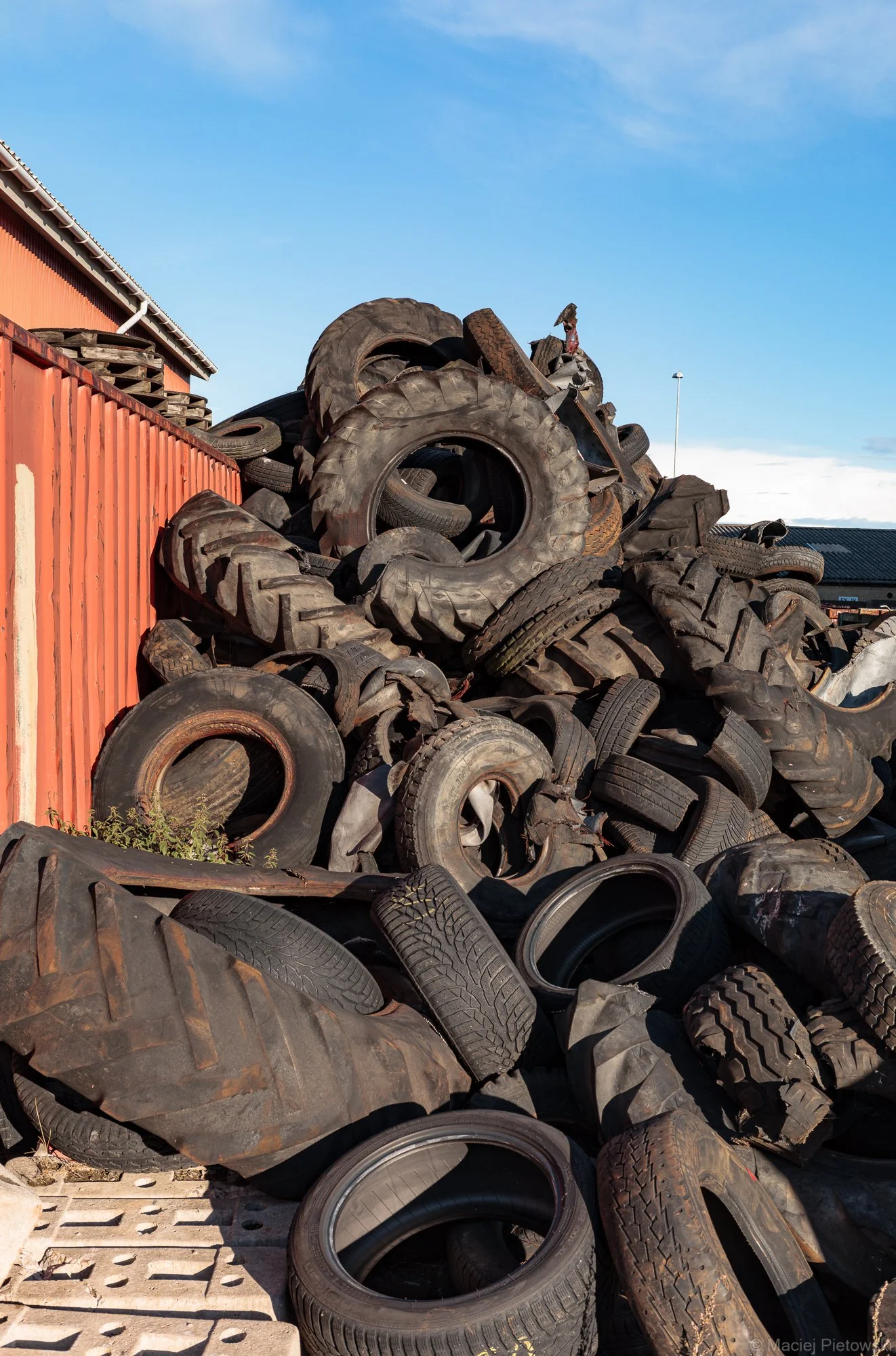 A pile of discarded tires stacked next to an orange building with blue sky in the background.