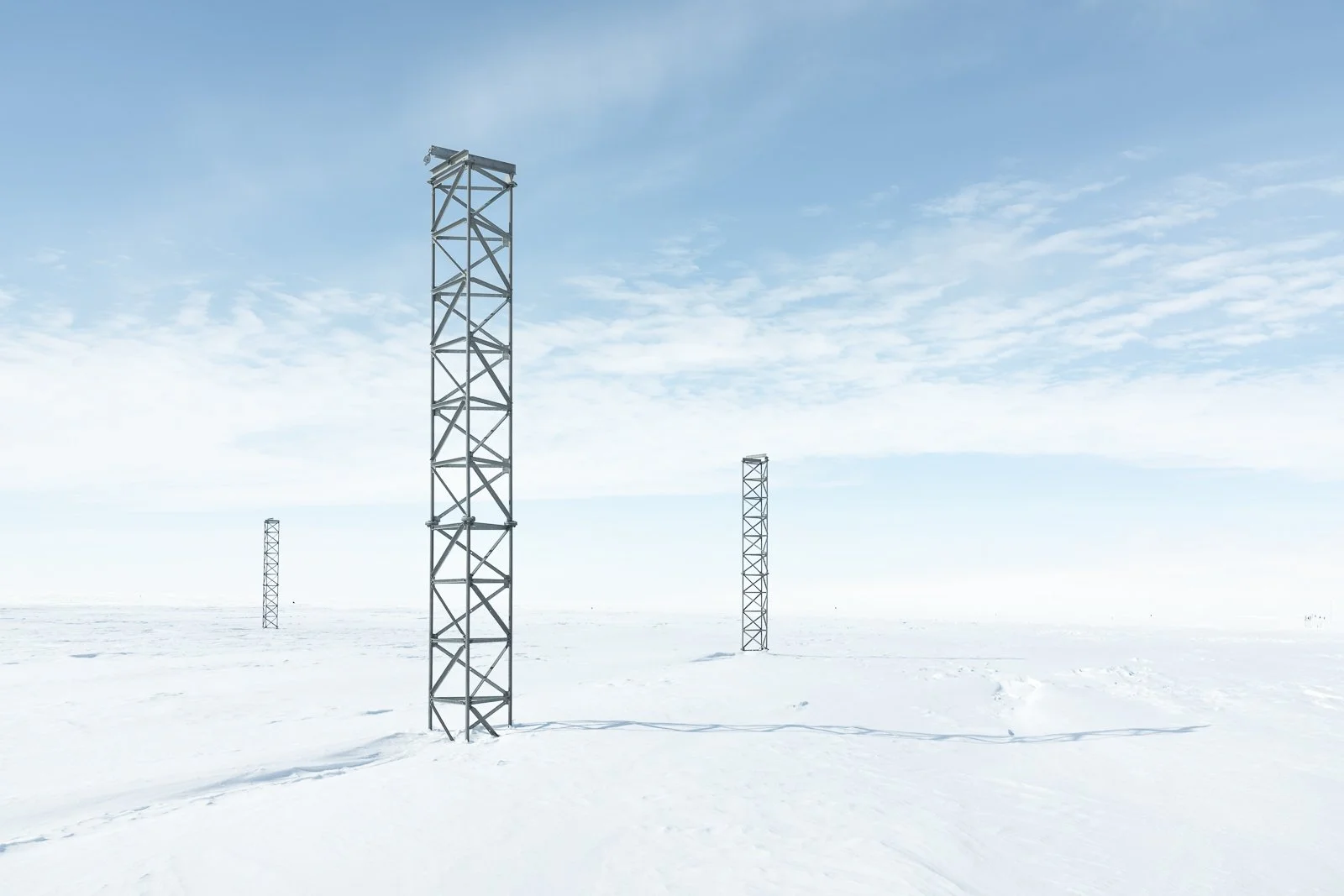 Four tall metal towers in a snow-covered landscape under a partly cloudy sky.