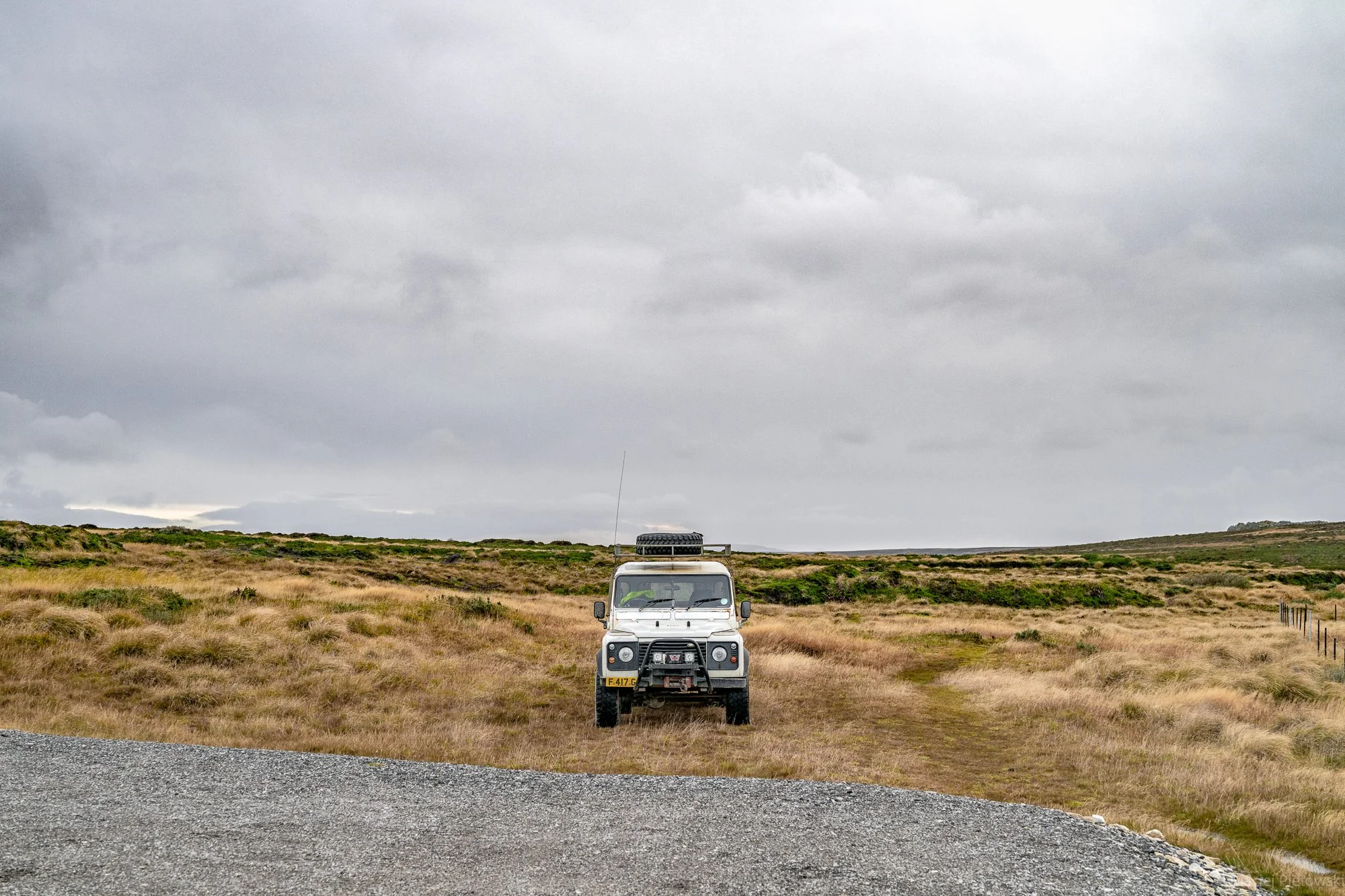 A white off-road vehicle parked in an open grassy landscape under a cloudy sky.