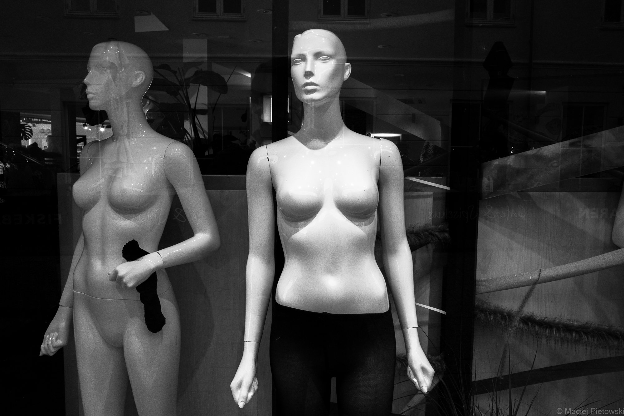Black-and-white photo of three mannequin torsos in a store window, with a focus on the middle female mannequin facing forward and the two other mannequins to the sides, one in profile and one facing forward.