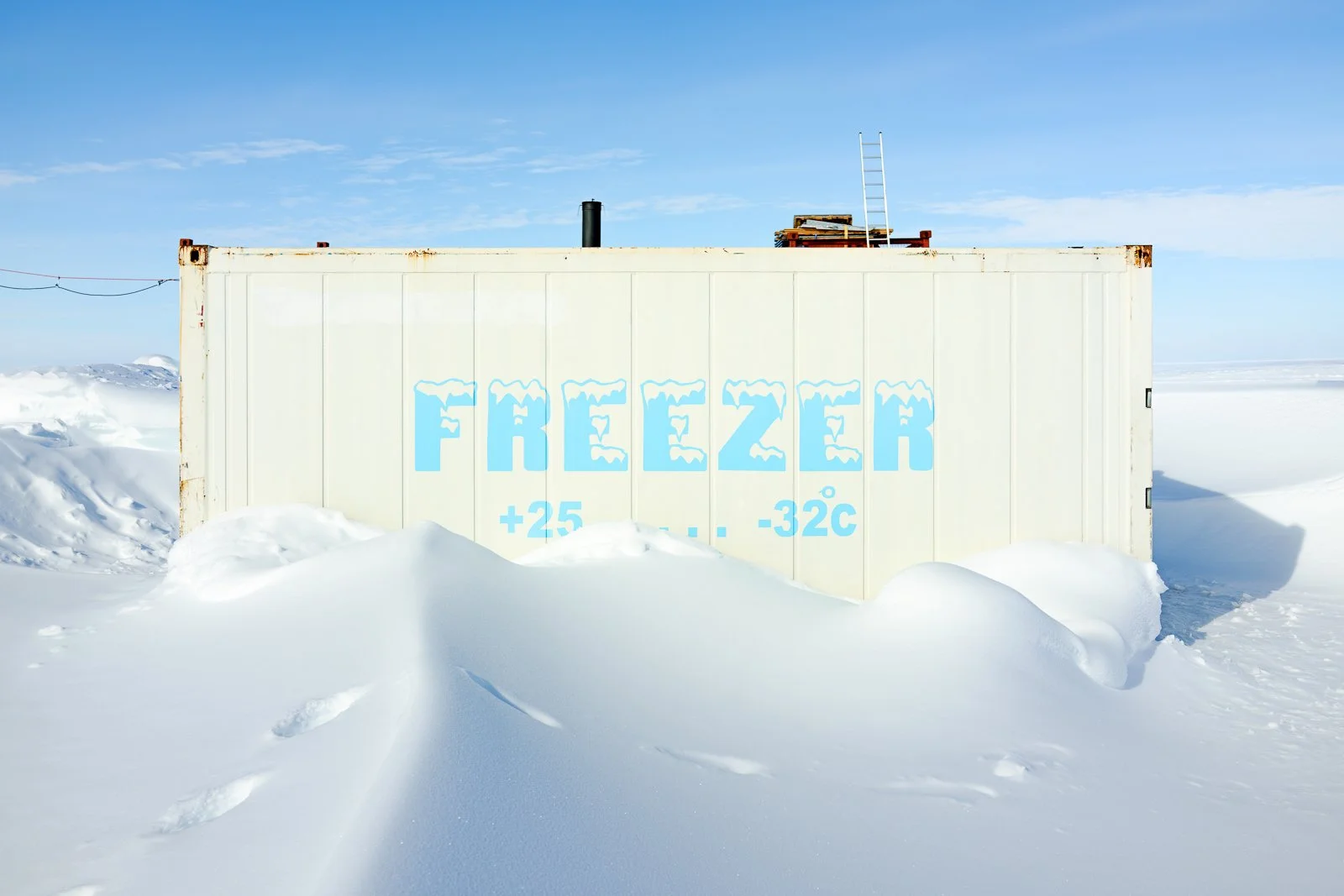 A white storage container in a snowy landscape with the word 'FREEZER' painted in ice blue on the side, along with temperature information of +25°C to -32°C.
