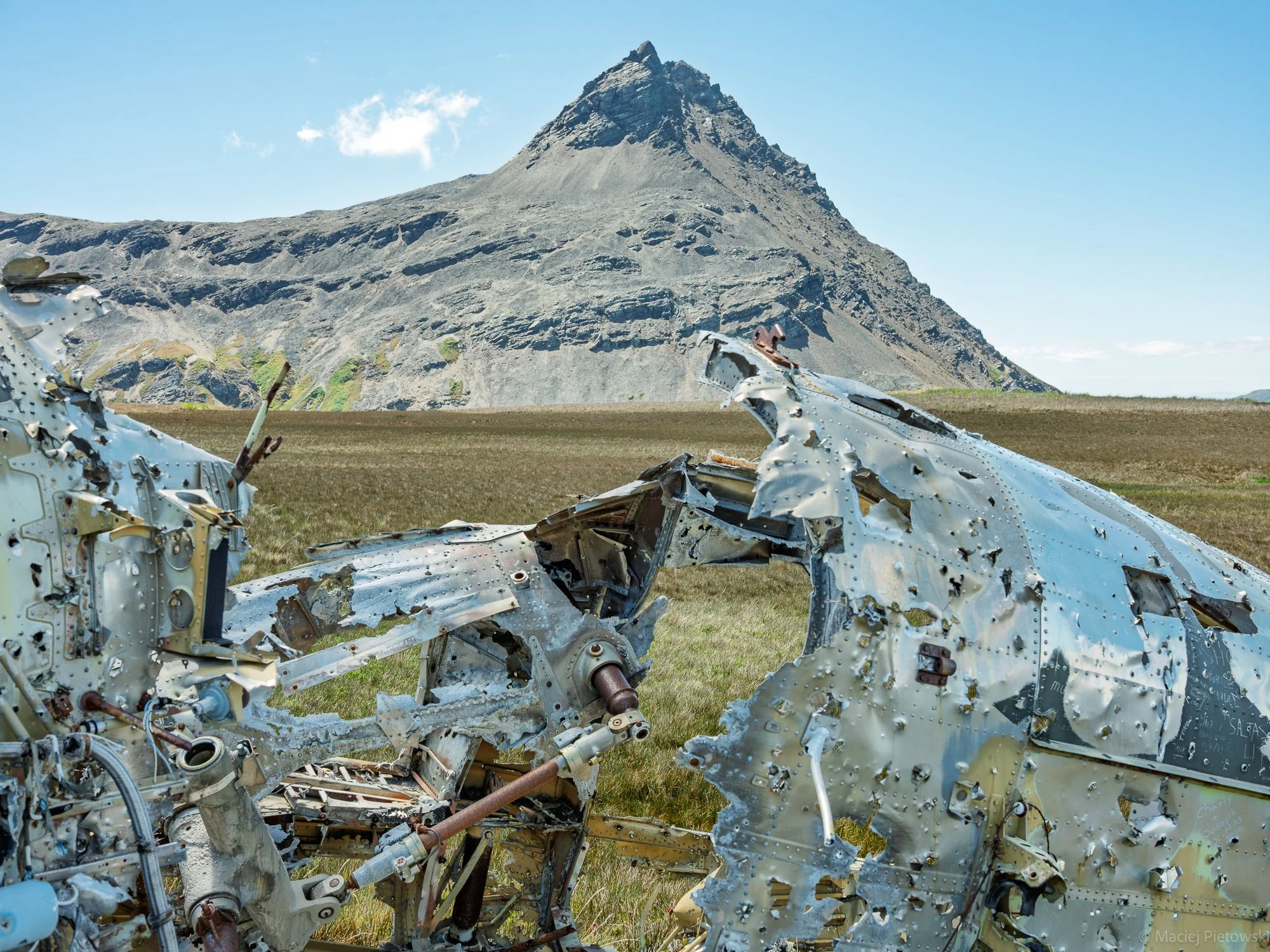 Ruins of an airplane with a mountain in the background, under a clear blue sky.