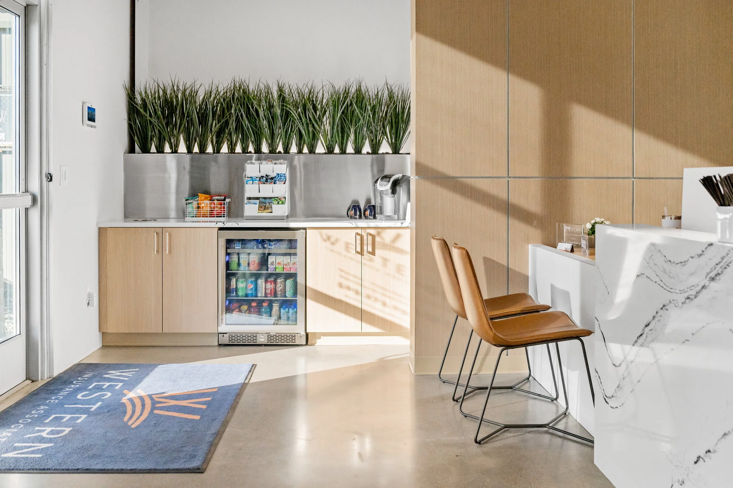 Western Insurance office area with a white marbled counter, brown chairs, a barista station with green plants, snack and beverage fridge